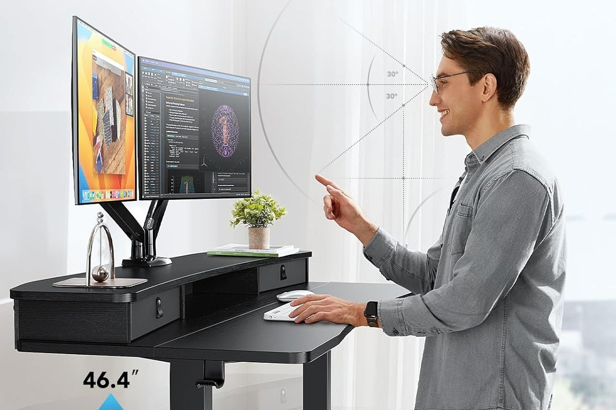 Man working at an adjustable standing desk with dual monitors and ergonomic setup.