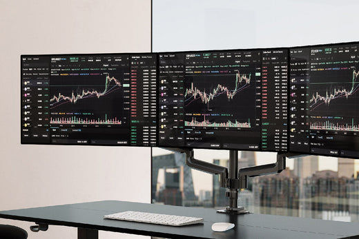 A modern desk setup with triple monitors displaying financial charts and graphs